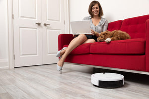 Woman registering for bObi's warranty while bObi Classic robotic vacuum sweeps under the couch.